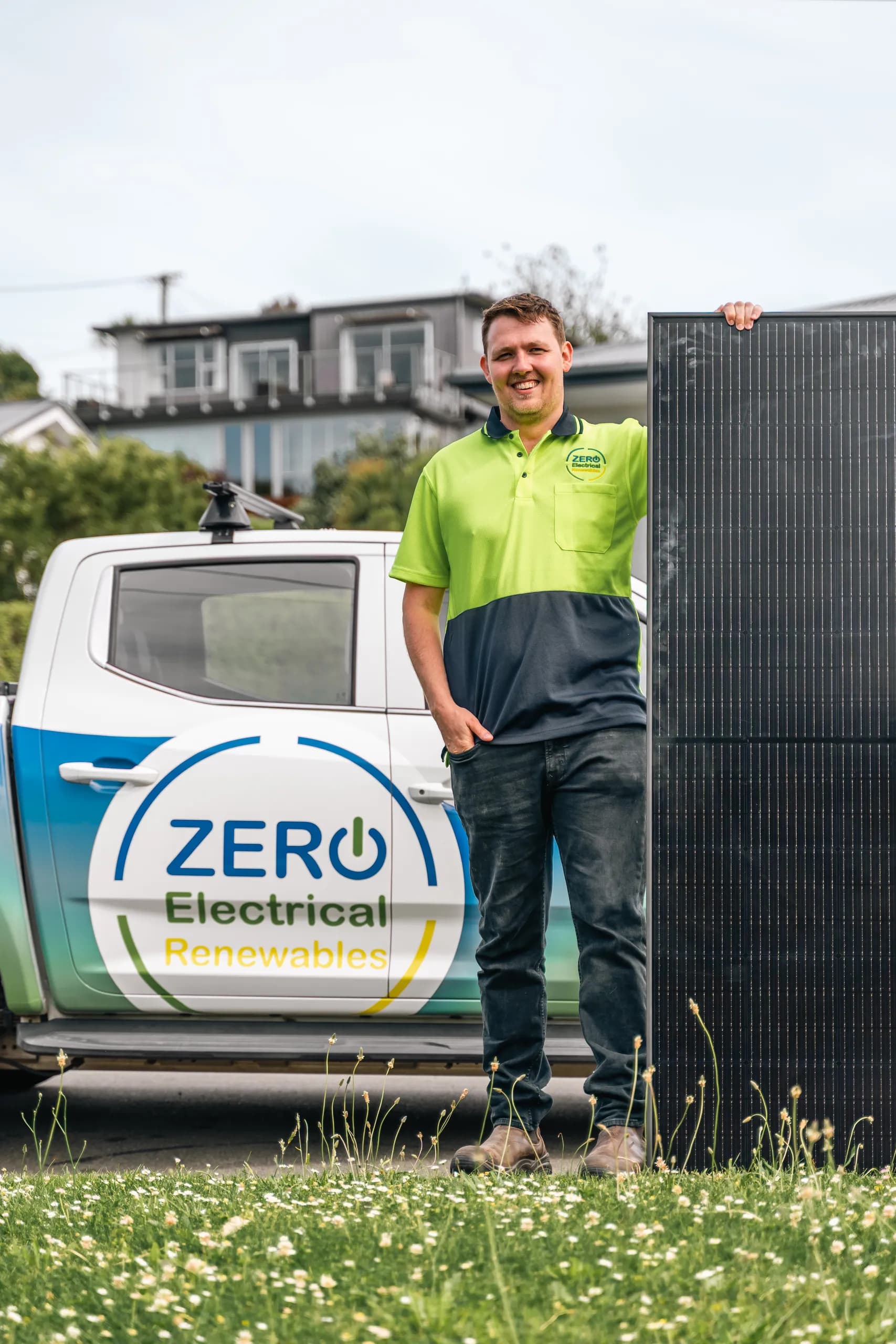 Portrait of a smiling ZERO electrician in hi-vis holding a solar panel next to the branded company ute.