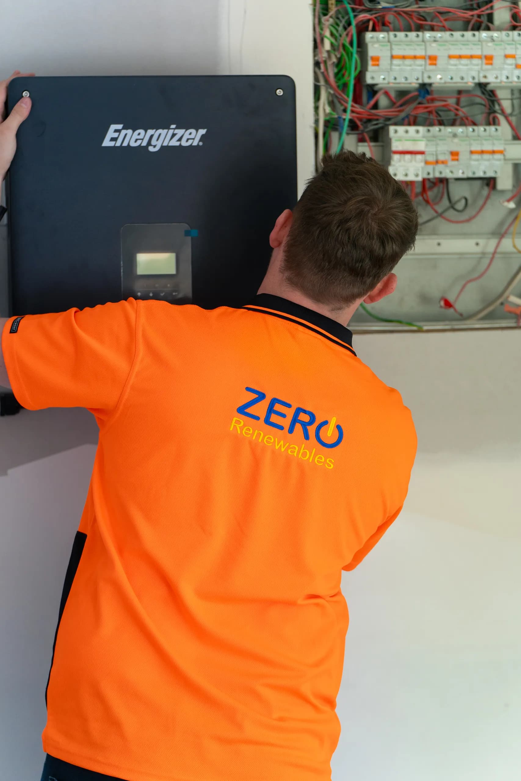 Close view of a technician mounting an Energizer inverter next to a switchboard with breakers and coloured wiring.