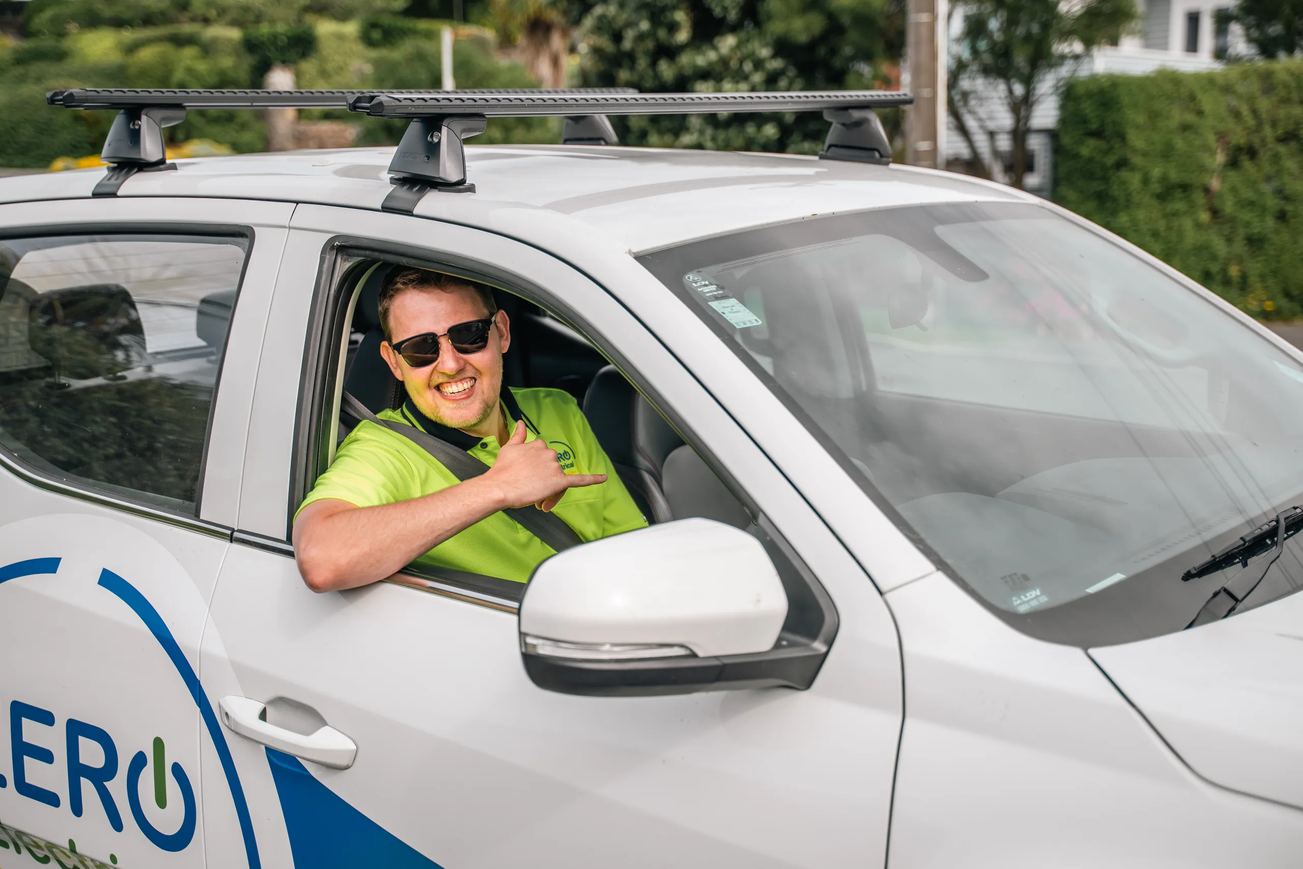 A ZERO electrician in hi-vis and sunglasses leans from the driver's window of the branded ute giving a shaka sign.